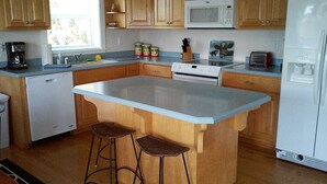 Una cocina con armarios de madera, un refrigerador blanco, un microondas, una estufa y una cafetera. Hay dos taburetes en la isla.