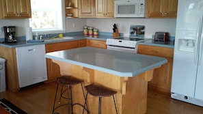 A kitchen with wooden cabinets, a white refrigerator, a microwave, a stove, and a coffee maker. There are two stools at the island.