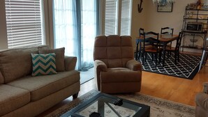 Una sala de estar con sofá, sillón, mesa de centro y comedor con sillas y una araña.