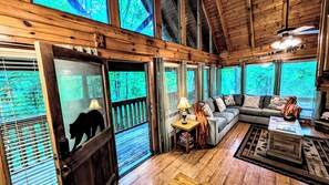 A cabin interior with a wooden ceiling, a sofa, a coffee table, and a fireplace.