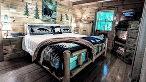 Een knus slaapkamer in blokhutstijl met een houten bed, een stenen openhaard en een televisie waarop 'Playful Paws' te zien is.