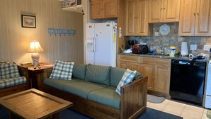 Un soggiorno accogliente con un divano in legno, un tavolino da caffè e una lampada. Adiacente al soggiorno si trova una cucina con mobili in legno, un frigorifero e una lavastoviglie.