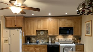 Cucina con mobili in legno, frigorifero, microonde, piano cottura e ventilatore a soffitto.