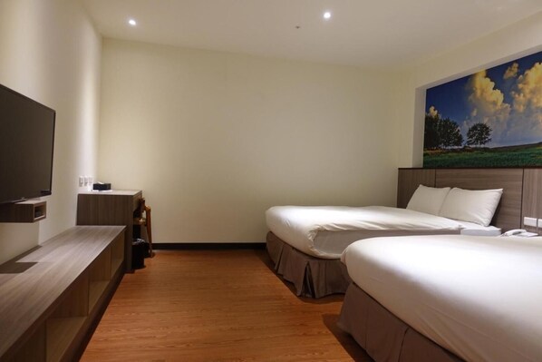 Habitación de hotel con dos camas, un televisor de pantalla plana, un escritorio de madera y un cuadro de un paisaje en la pared.