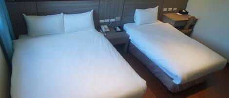 Habitación de hotel con dos camas, una mesita de noche con teléfono y vista al mar a través de una ventana.