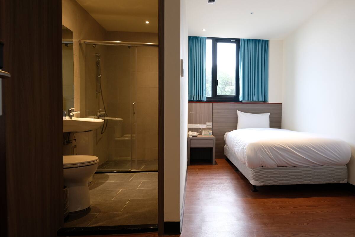 A hotel room with a shower, toilet, bedside table, and a bed.
