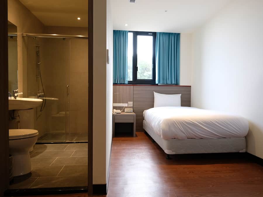 Ein Hotelzimmer mit Dusche, Toilette, Nachttisch und einem Bett.