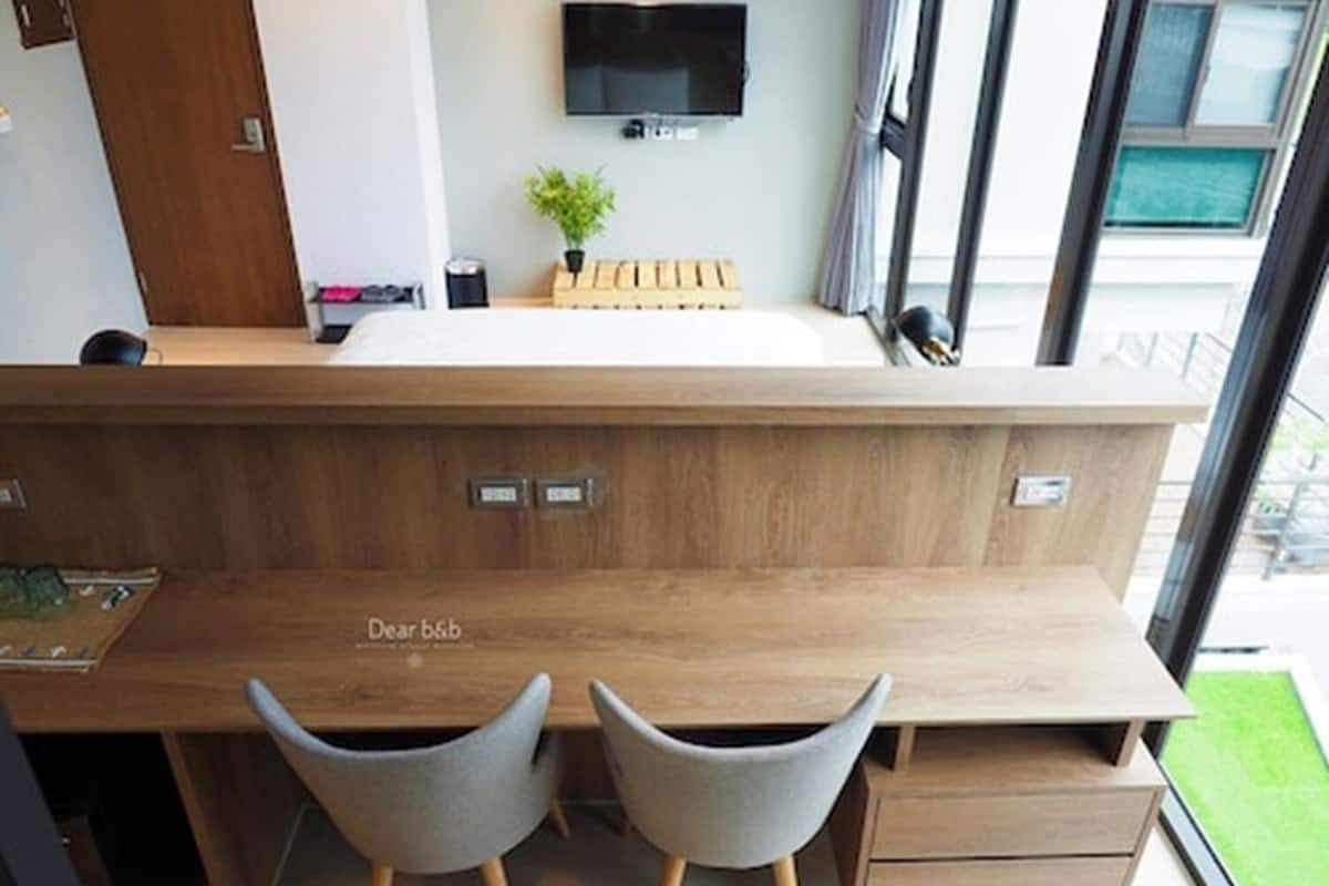 Een moderne keuken met een houten aanrecht, twee grijze stoelen en een tv die boven het aanrecht is bevestigd.
