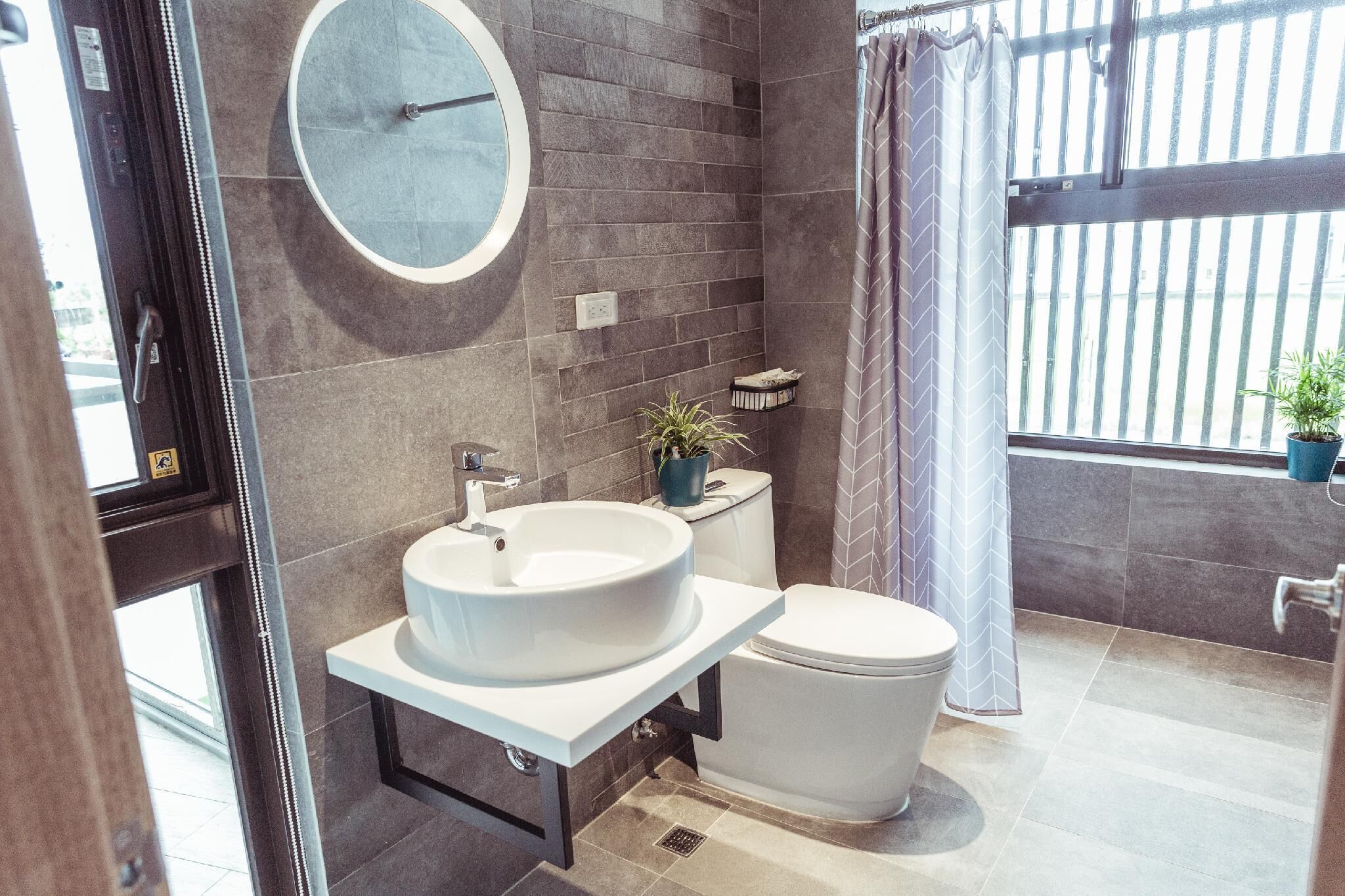 Un baño moderno con un espejo redondo, un lavabo blanco y un inodoro.