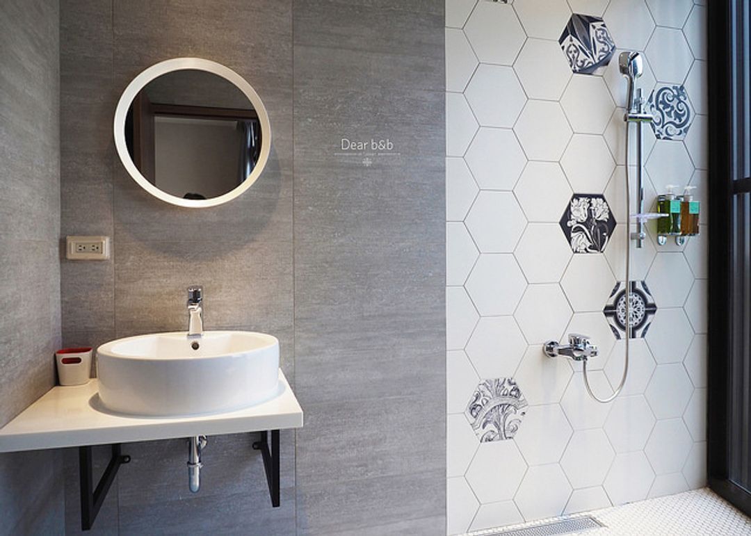 Un baño con un espejo redondo, un lavamanos blanco y una zona de ducha con azulejos hexagonales.