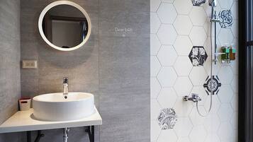 Un baño con un espejo redondo, un lavamanos blanco y una zona de ducha con azulejos hexagonales.