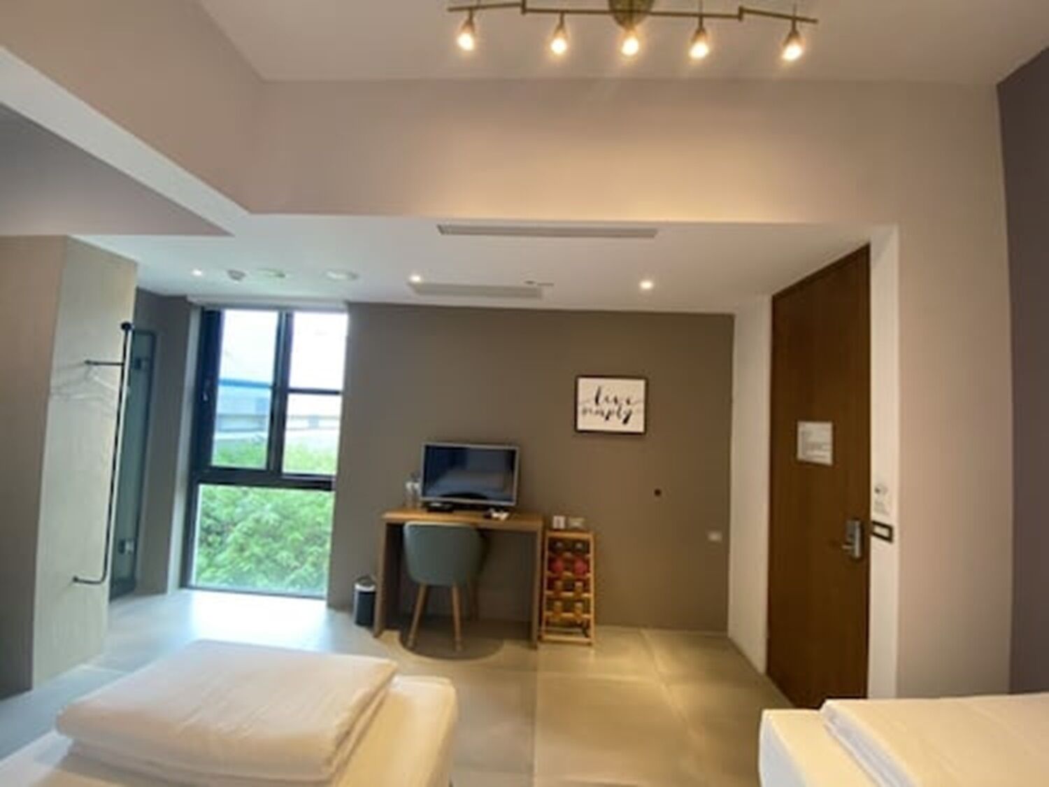 Una habitación de hotel moderna con dos camas, un escritorio con ordenador, un televisor y un amplio ventanal con vistas a zonas verdes.