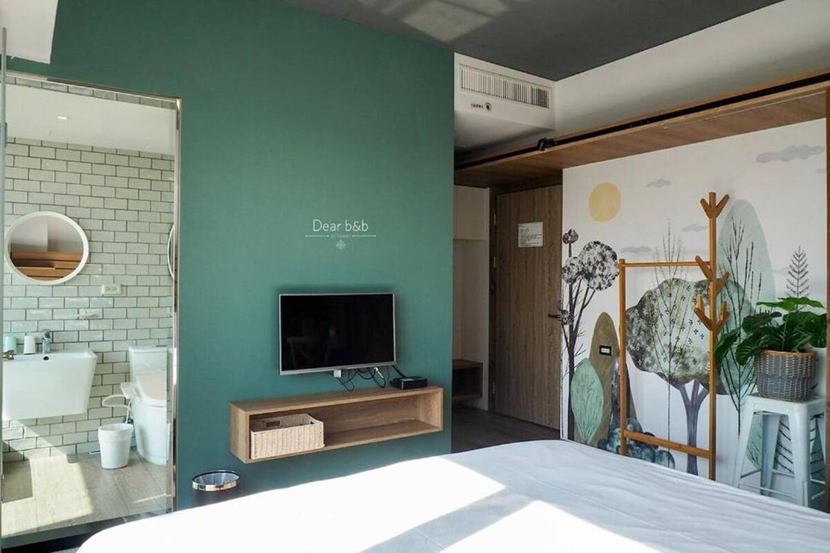 Een moderne hotelkamer met een groot bed, een televisie, een spiegel, een wastafel en een muur met een 'Dear b&b' bord.