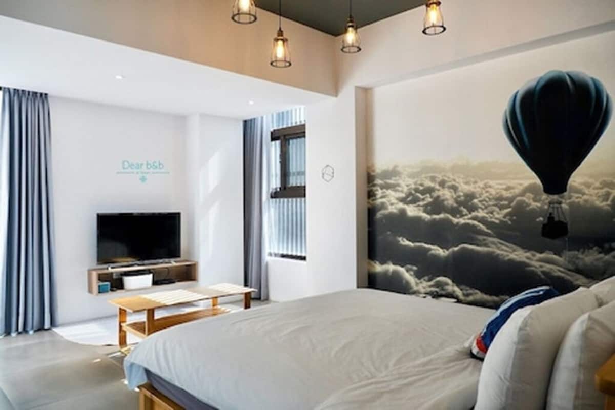 Een moderne hotelkamer met een groot bed, een flatscreen-tv, een bureau en een muurschildering van wolken met een luchtballon.