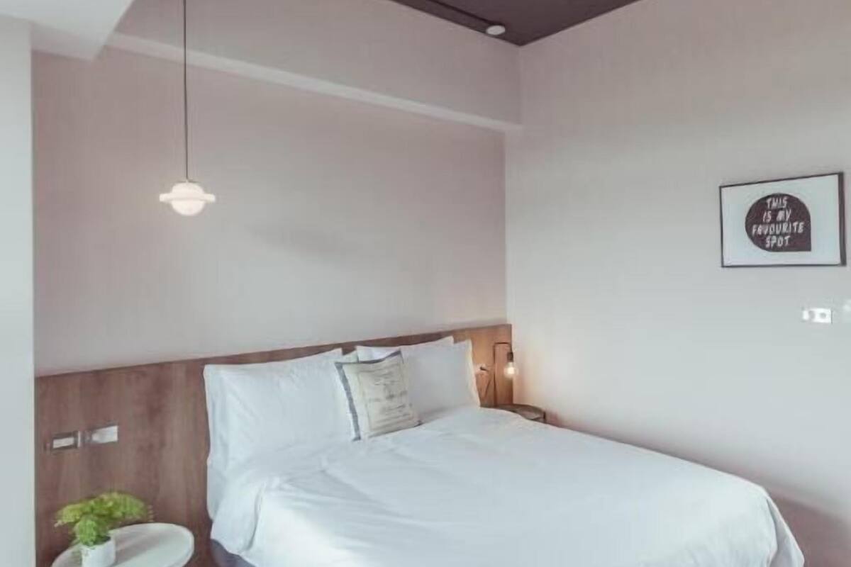 Een moderne slaapkamer met een groot bed, een rond nachtkastje met een plant, en een plafondlamp.