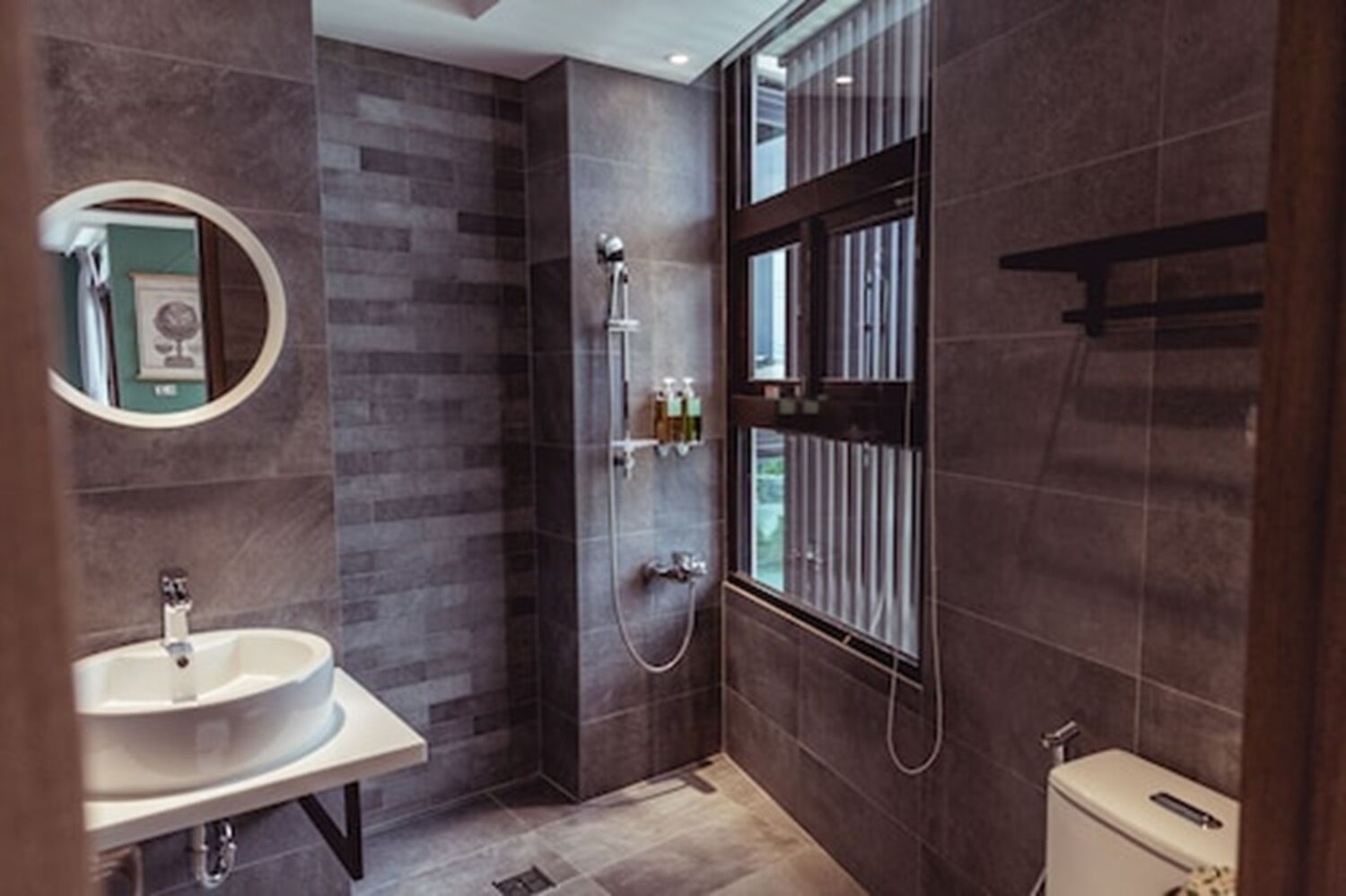 A modern bathroom with a large mirror, a sink, a shower, and a toilet.