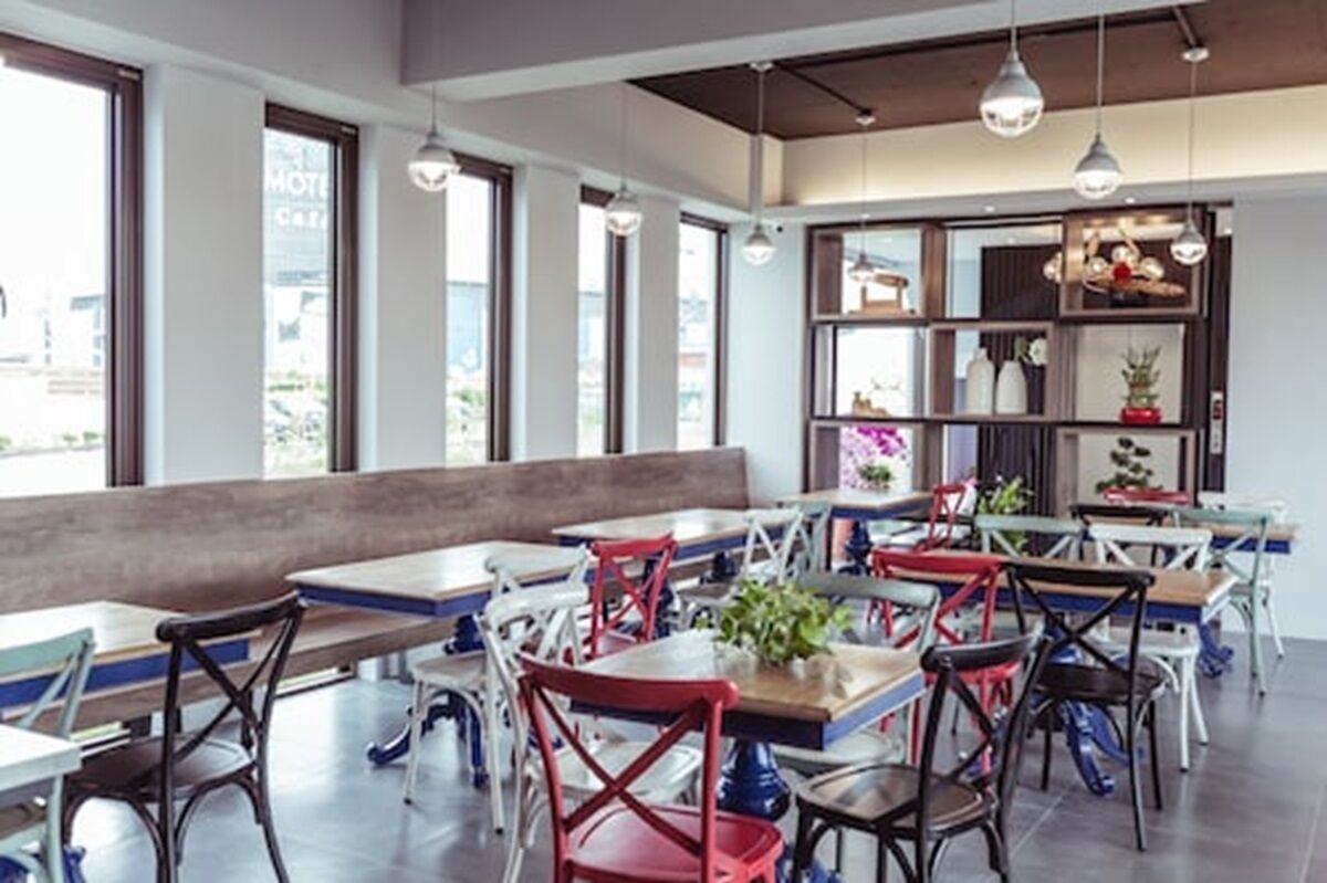 Um restaurante moderno com pé-direito alto, luminárias pendentes e diversos tipos de assentos, incluindo mesas e bancos.