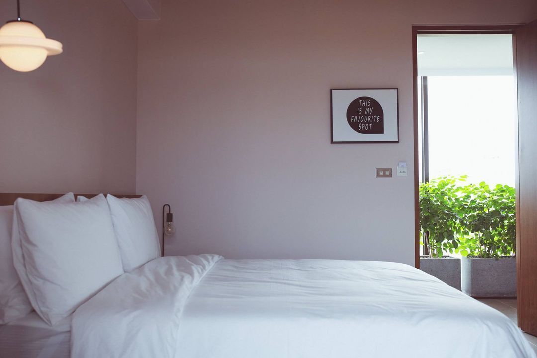 Una cama bien tendida en una habitación con un cartel en la pared y vista a zonas verdes al exterior.