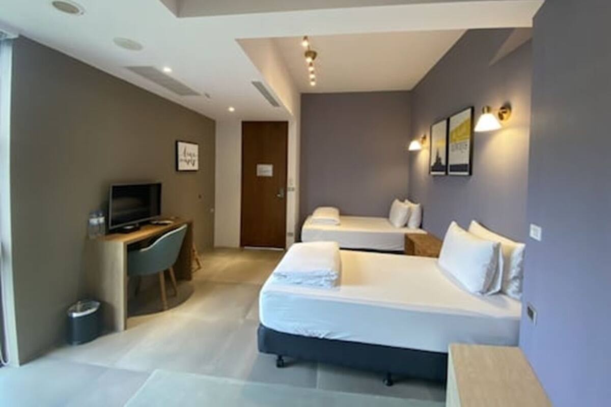 Een hotelkamer met twee bedden, een bureau met een televisie, en een deur naar een andere kamer.