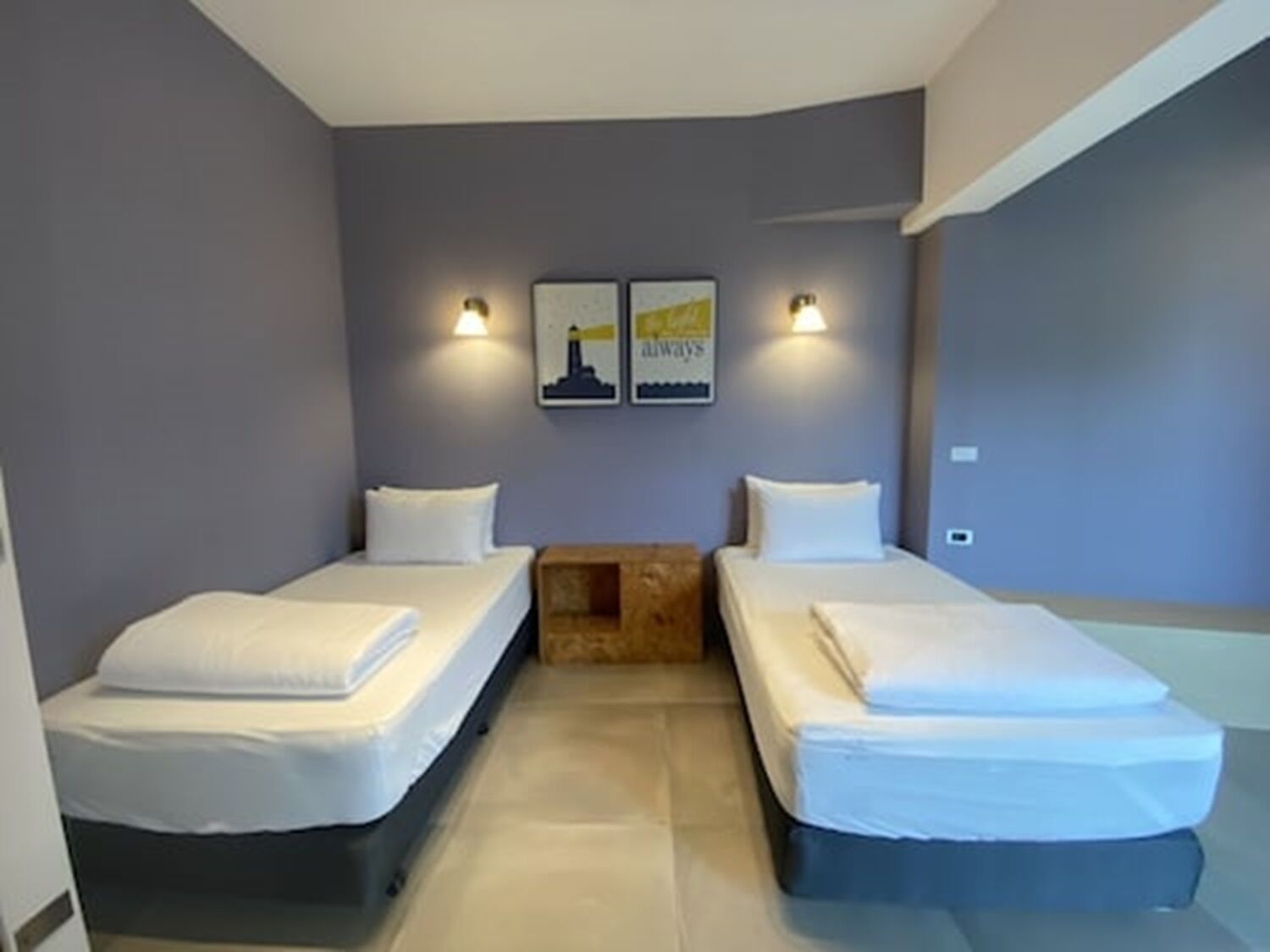Una habitación con dos camas, una mesita de madera y dos lámparas fijadas a la pared.