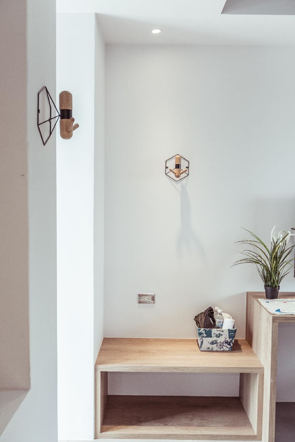 Una habitación minimalista con un banco de madera, una lámpara hexagonal de pared y una planta en maceta.