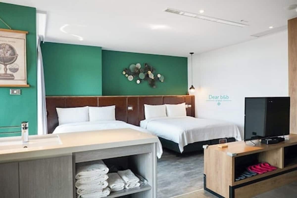 Hotelkamer met twee bedden, een bureau met een computer, een televisie en een kunstwerk aan de muur.