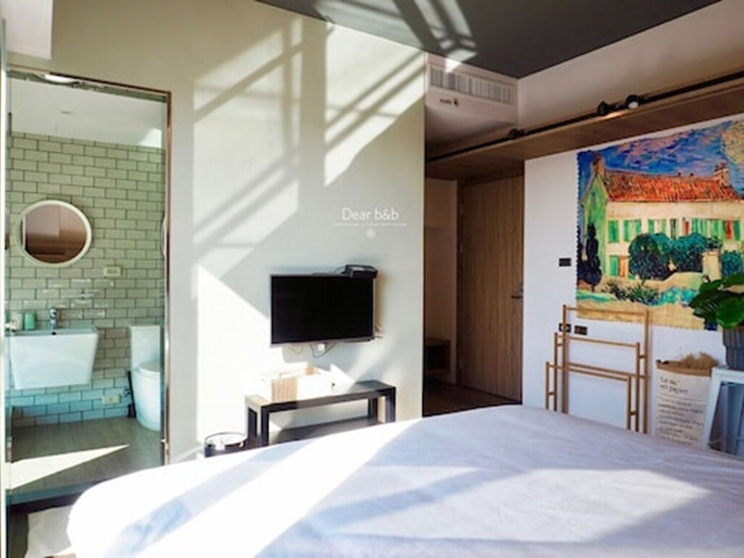 Un dormitorio moderno con una cama, televisión, baño con espejo y lavamanos, y un cuadro en la pared.
