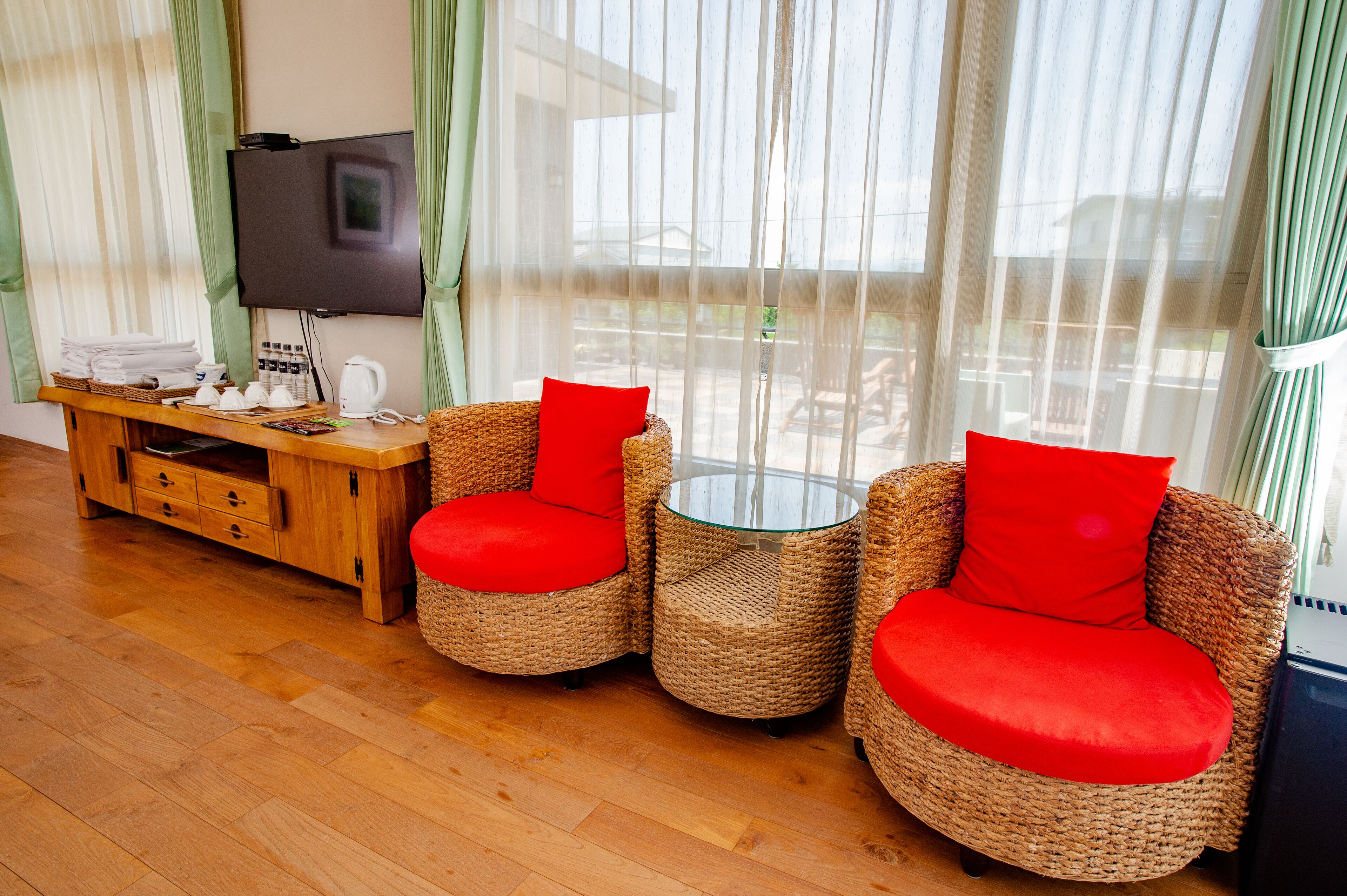 A room with wicker furniture, a flat-screen TV, and a wooden cabinet with towels and toiletries.