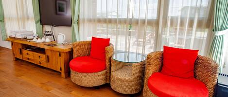 A room with wicker furniture, a flat-screen TV, and a wooden cabinet with towels and toiletries.