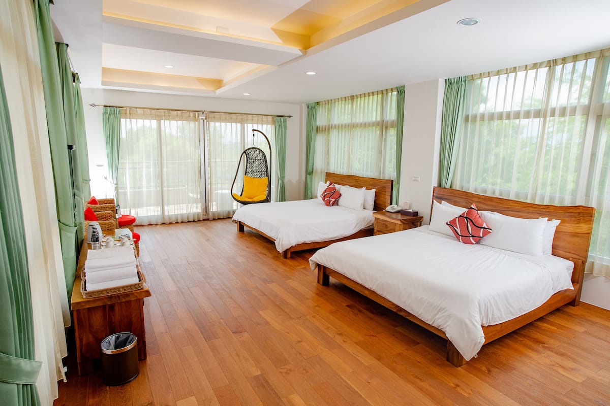 A hotel room with two beds, a wooden floor, a hanging chair, and a small table with a basket of towels.