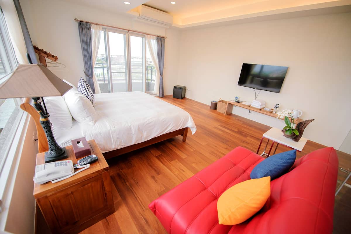 A hotel room with a bed, a red sofa, a TV, and a window with curtains.