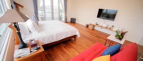 Una habitación de hotel con una cama, un sofá rojo, un televisor y una ventana con cortinas.