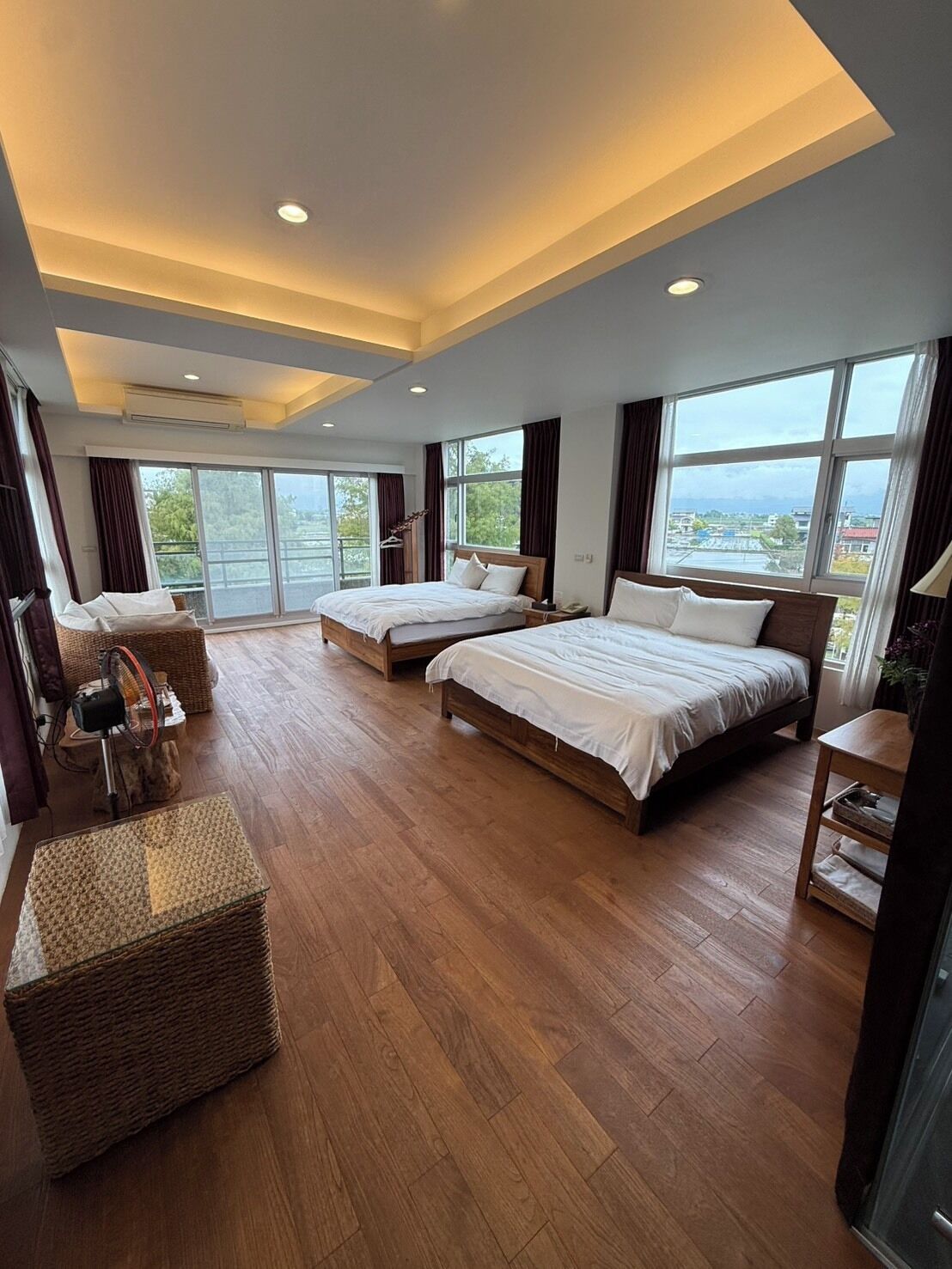 A spacious bedroom with two beds, large windows, and a balcony.
