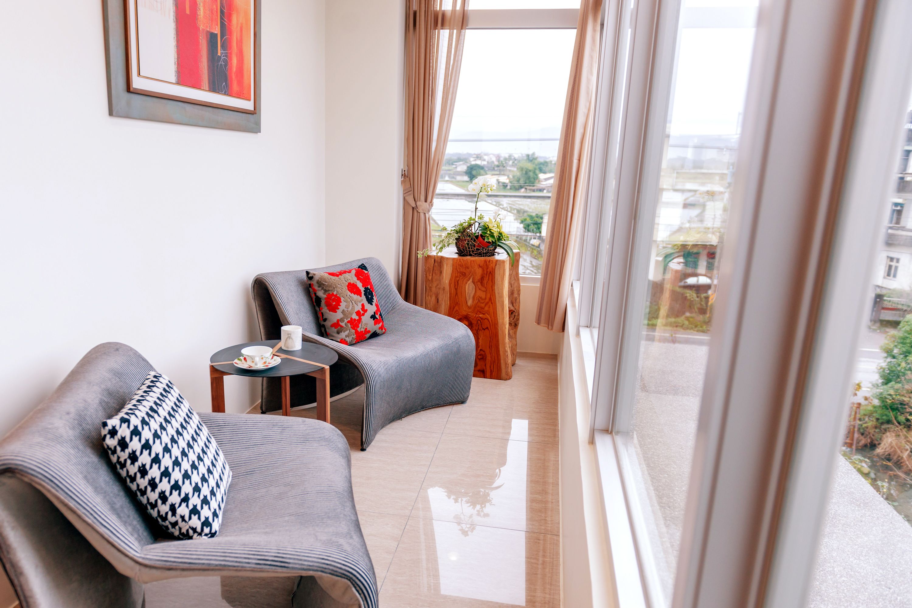 A modern living room with two grey sofas, a small wooden table, and a view of a cityscape through large windows.