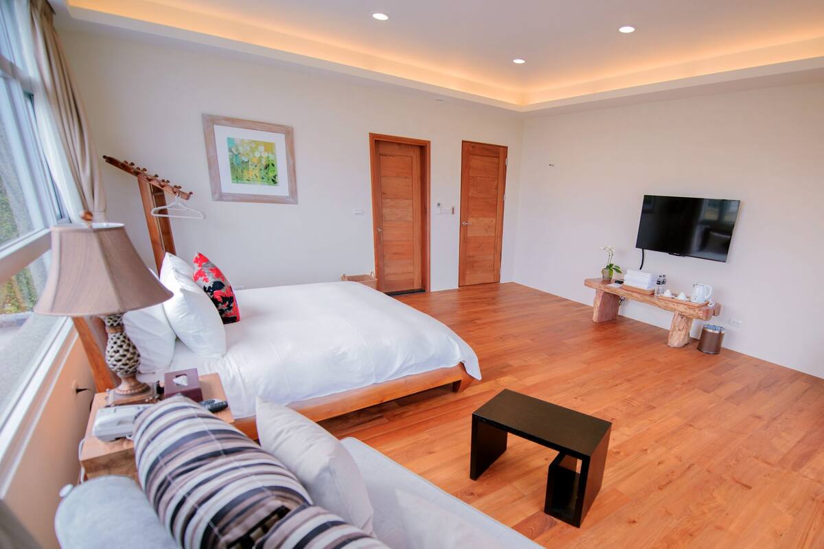 A hotel room with a bed, a sofa, a TV, and wooden flooring.