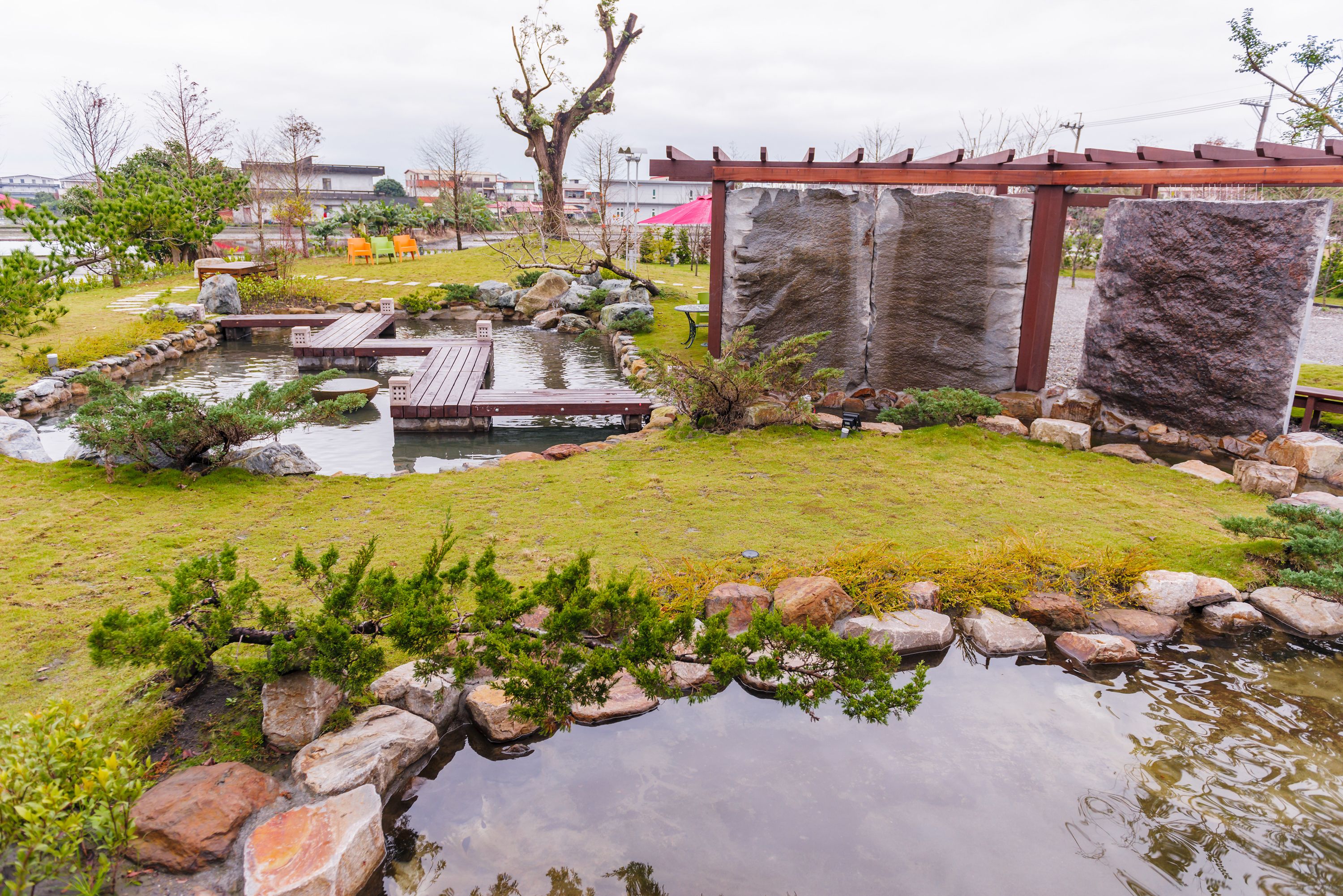 A serene garden with a pond, wooden deck, and stone structures.