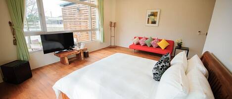 Un dormitorio con una cama grande, un televisor sobre un soporte de madera, un sofá rojo y una ventana con cortinas.
