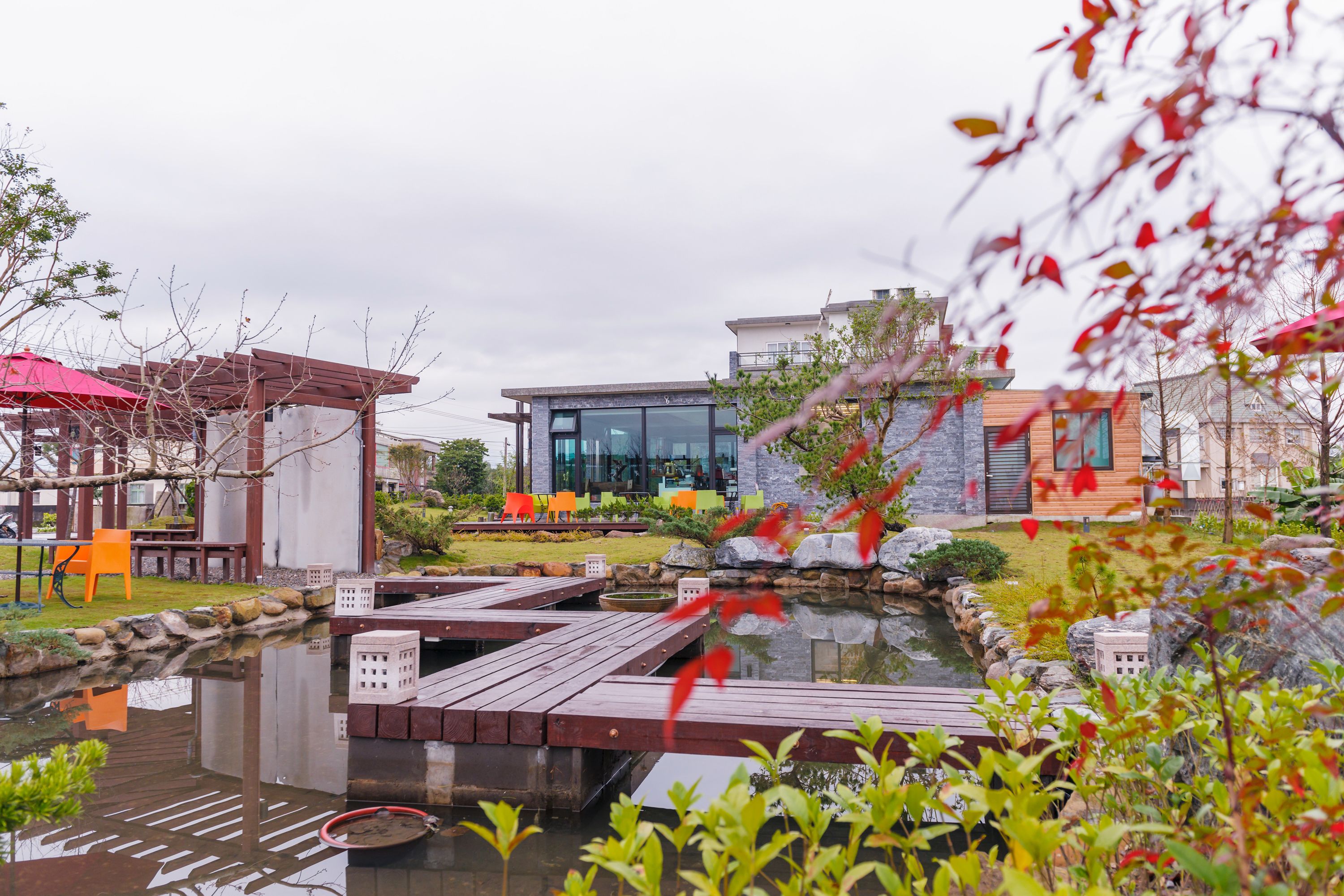 A modern outdoor area with a wooden deck, a small pond, and a seating area with colorful chairs.