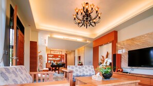 Una sala de estar moderna con muebles de madera, una lámpara de araña, un televisor y una cocina al fondo.