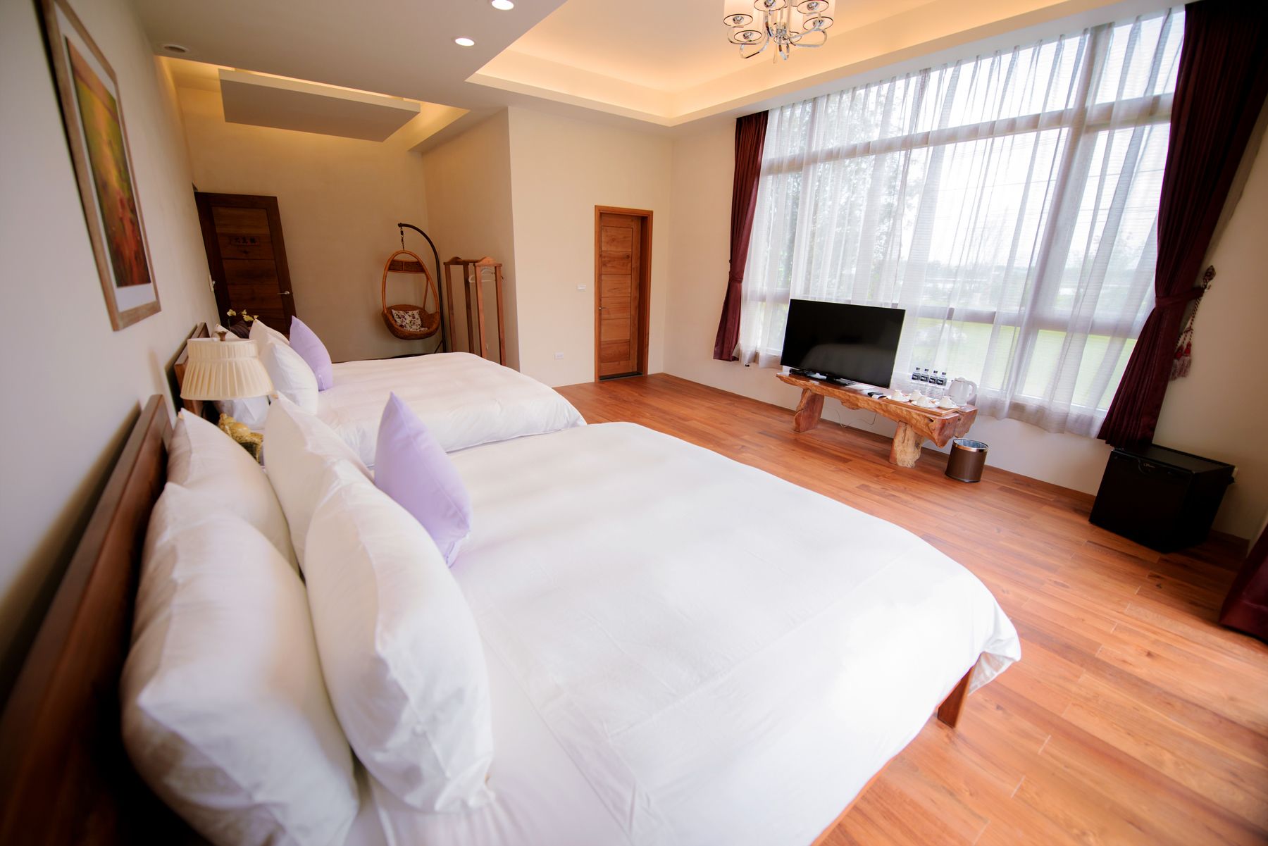 Een ruime slaapkamer met twee grote bedden, een televisie en een houten bijzettafeltje.