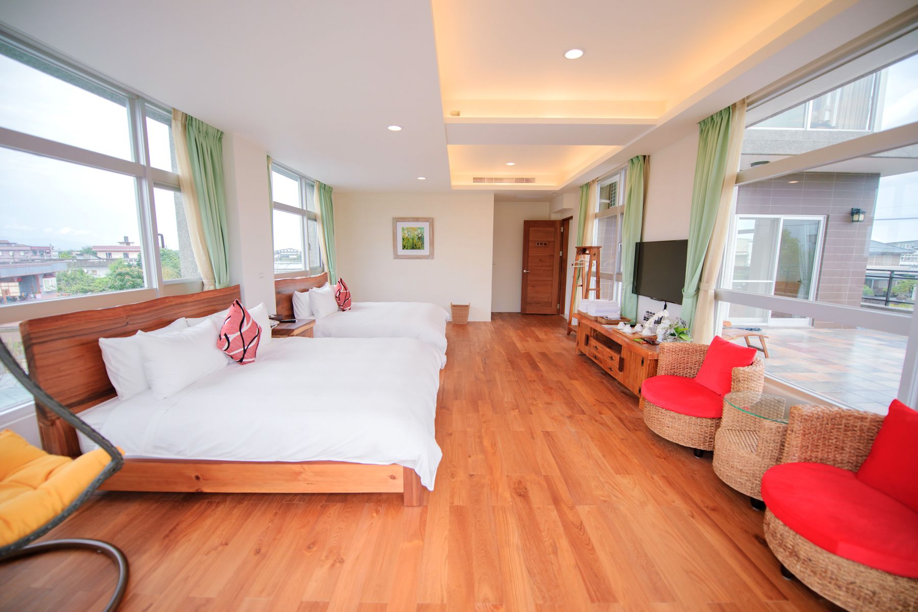 Habitación de hotel con dos camas, televisión, balcón con mobiliario de mimbre y ventanas amplias.