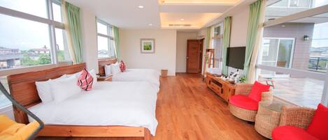 Habitación de hotel con dos camas, televisión, balcón con mobiliario de mimbre y ventanas amplias.