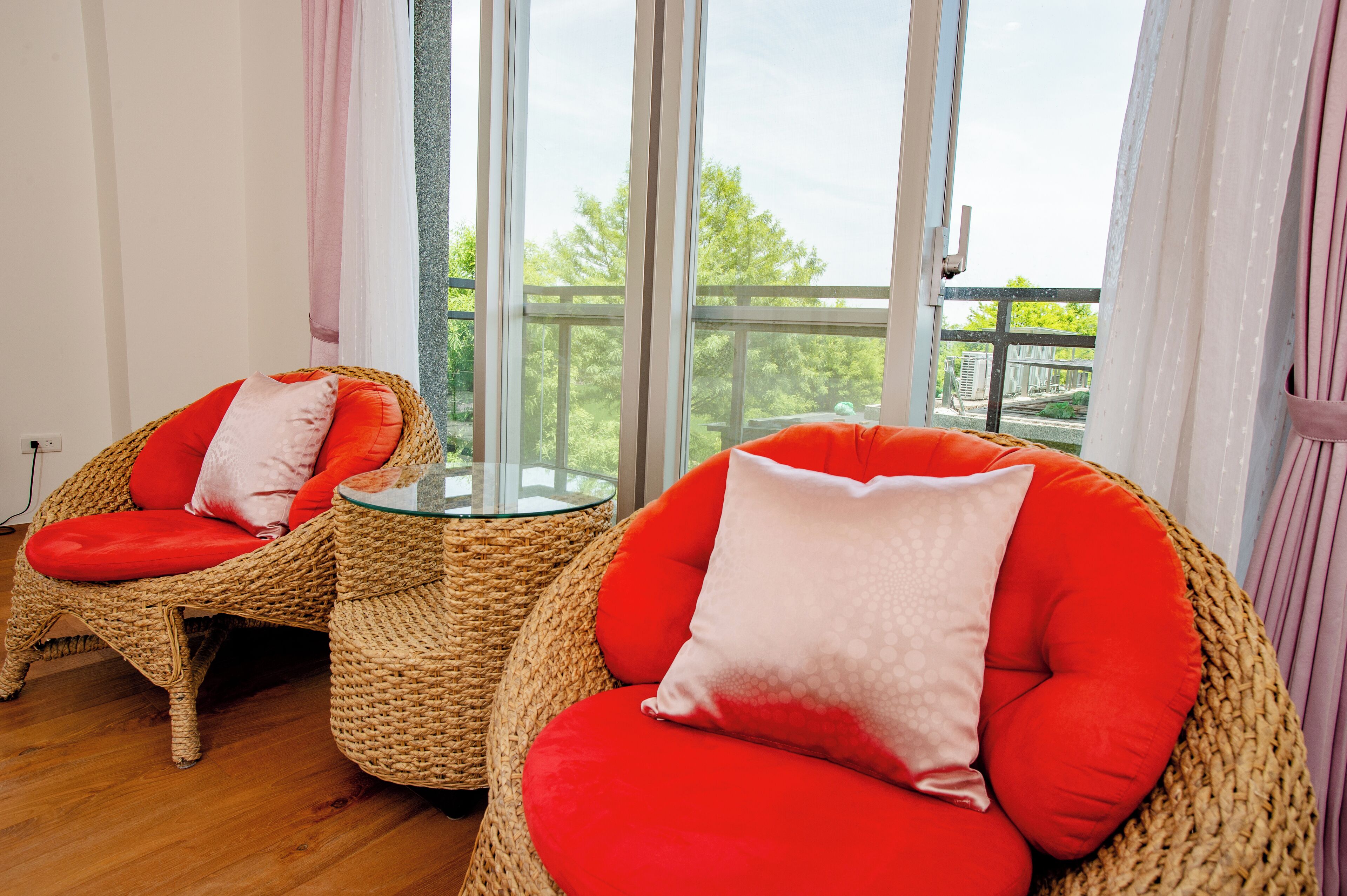 Un balcón con sillas de mimbre y una mesa de cristal, con vistas a un paisaje verde.