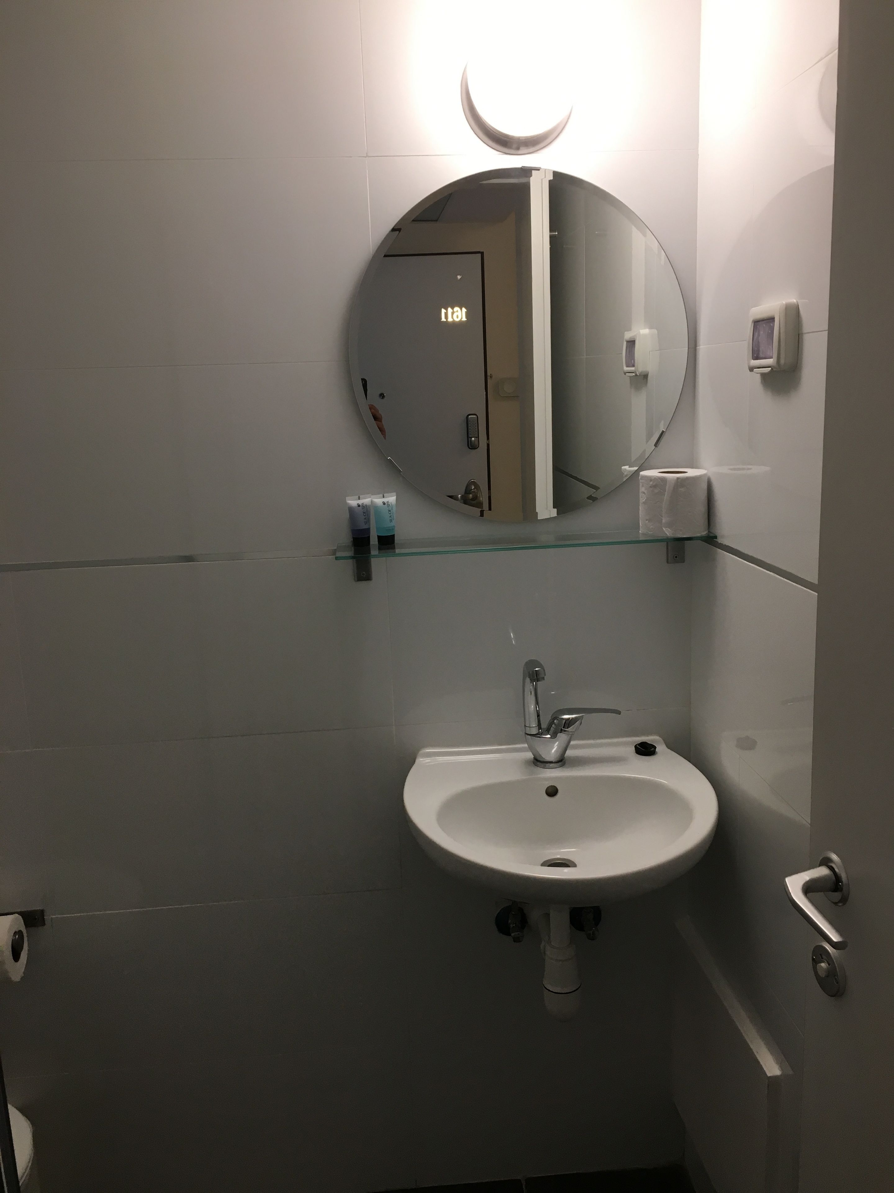 Un baño con un espejo redondo, un lavamanos y un inodoro.