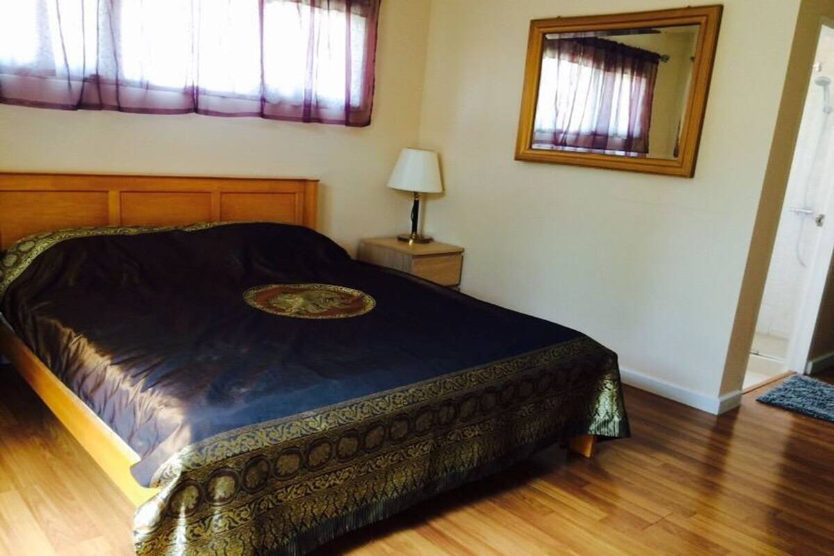 A bedroom with a large bed, a nightstand with a lamp, a mirror, and a door.