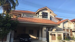 A two-story house with a tiled roof, a car parked in the driveway, and a gated entrance. - Bann Dao (Lam Luk Ka)