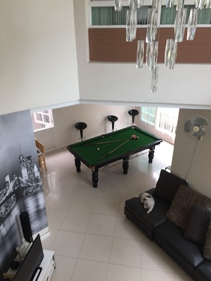 A pool table in a room with a sofa and a fan.