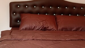 A bed with a brown headboard and matching pillows, a wall-mounted light fixture, and a patterned bedspread. - Suansuppachok Inn (Ongkharak)