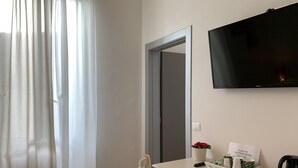 A hotel room with a bed, a desk with a chair, a television, and a window with curtains. - Affittacamere Il Borgo (Levanto)