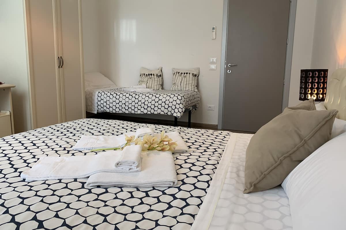 A hotel room with a bed, a bedside table, a lamp, and a door.